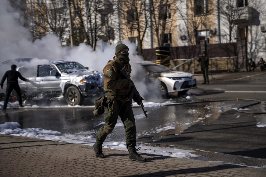 Ukrainian soldiers take positions outside a military facility as two cars burn, in a street in Kyiv, Ukraine, Saturday, Feb. 26, 2022. Russian troops stormed toward Ukraine&#039;s capital Saturday, an ...