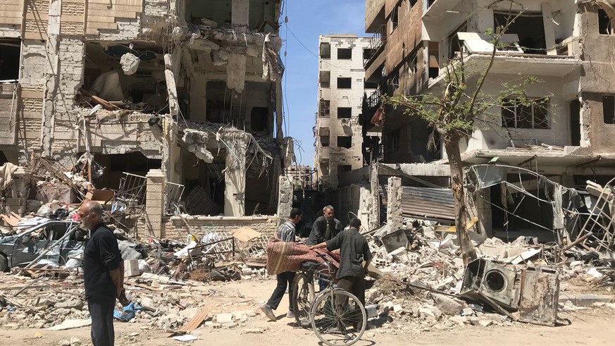 People stand in front of damaged buildings, in the town of Douma, the site of a suspected chemical weapons attack, near Damascus, Syria, Monday, April 16, 2018. Faisal Mekdad, Syria’s deputy foreign m ...