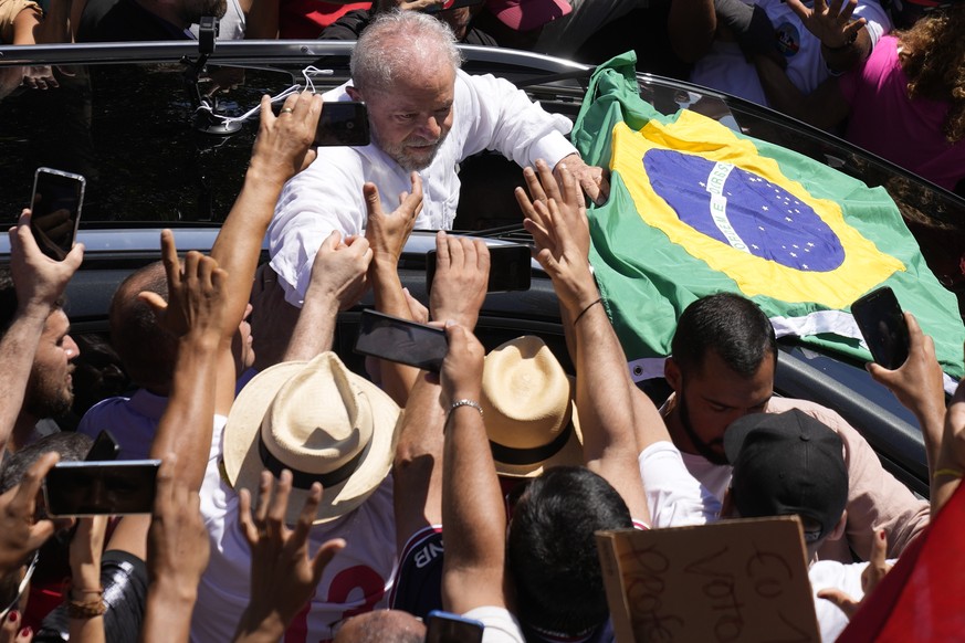 Former Brazilian President Luiz Inacio Lula da Silva, center, who is running for president again, hold hands with a supporter after voting in a presidential run-off election in Sao Paulo, Brazil, Sund ...