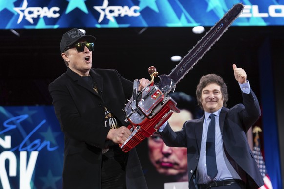 Elon Musk holds up a chainsaw he received from Argentina&#039;s President Javier Milei, right, as they arrive to speak at the Conservative Political Action Conference, CPAC, at the Gaylord National Re ...