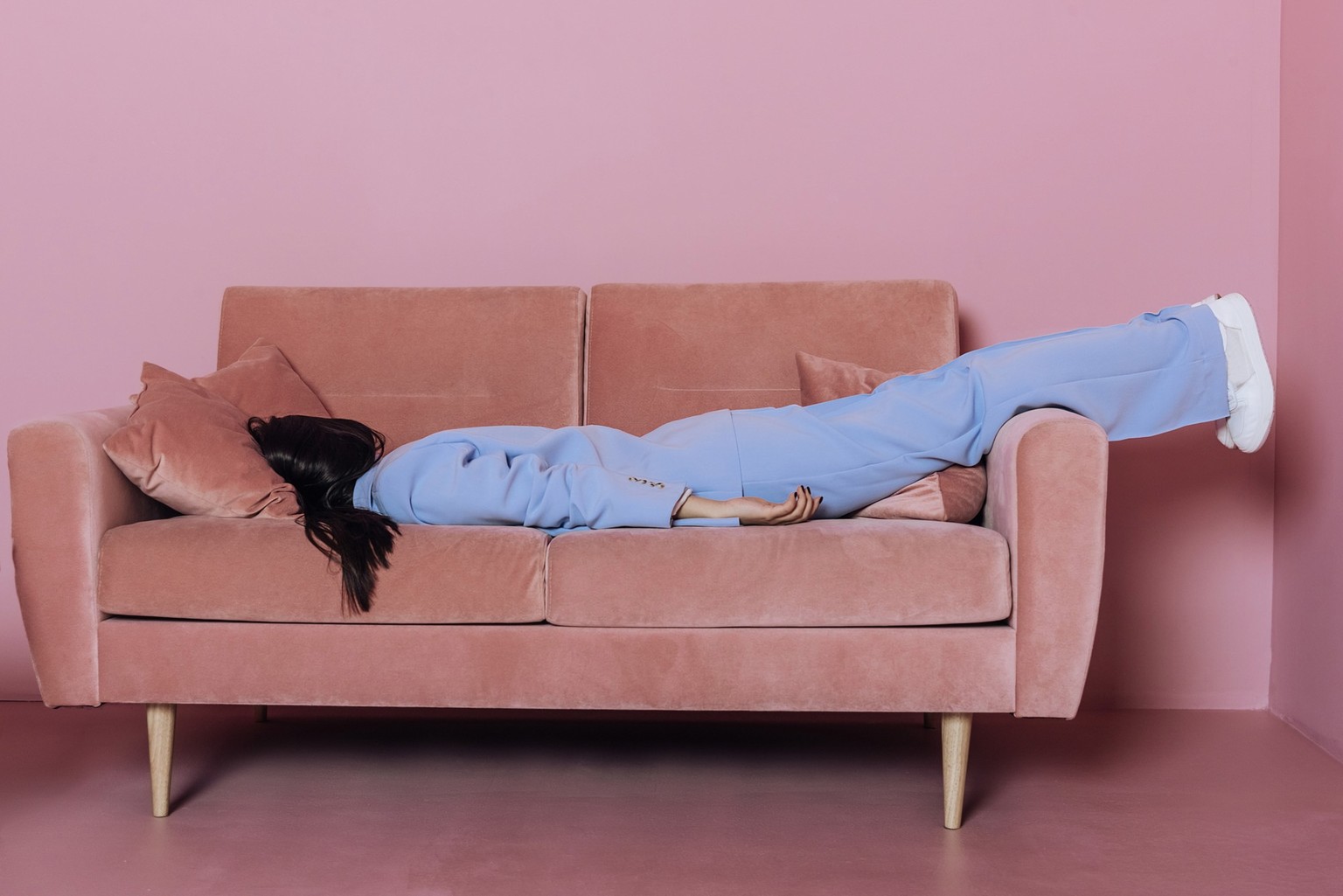 Creative portrait of a woman lying in a blue suit on a pink sofa. Fashion concept.