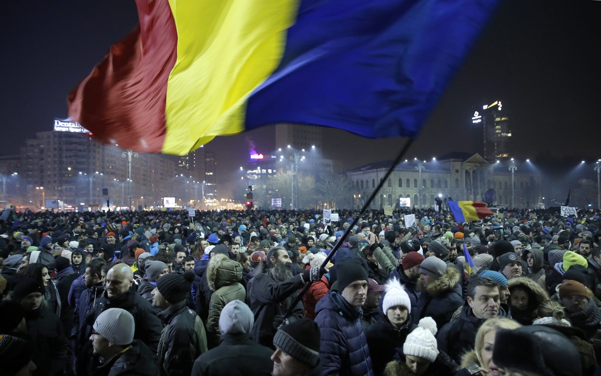 epaselect epa05763814 A Romanian man waves large-scale of the national flag as people shout anti-government slogans during a protest rally in front of government headquarters in downtown Bucharest, Ro ...
