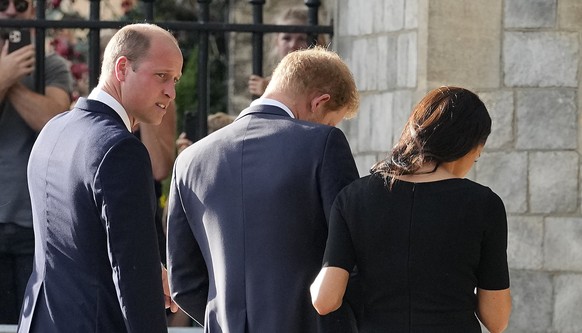 Prince William, left, watches Prince Harry and Meghan, Duchess of Sussex, as they view the floral tributes for the late Queen Elizabeth II outside Windsor Castle, in Windsor, England, Saturday, Sept.  ...