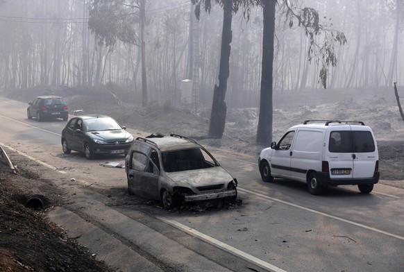 Cars drive past a burnt car on the road between Castanheira de Pera and Figueiro dos Vinhos, central Portugal, Sunday, June 18 2017. Raging forest fires in central Portugal killed more than 50 people, ...