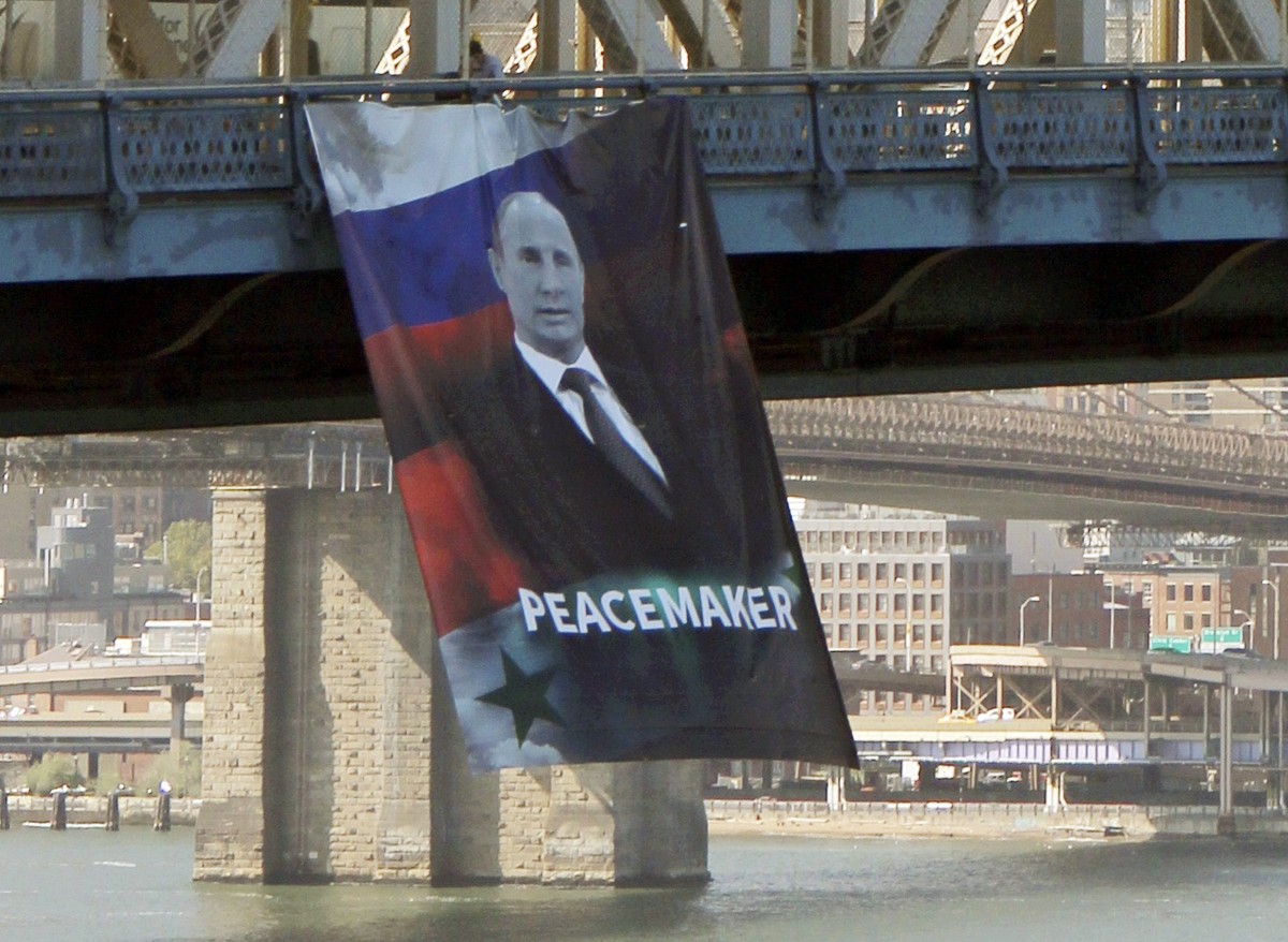 In this photo provided by Gothamist.com, a banner bearing an image of Russian President Vladimir Putin showing him with a Russian and Syrian flag as backdrop and labeling him a "peacemaker"  ...