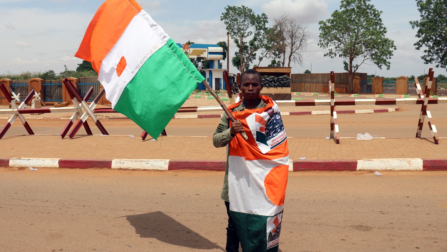 epa10824343 A supporter of the military junta displays a flag of Niger during a rally at at a roundabout leading to the French airbase during a rally in Niamey, Niger, 27 August 2023. The junta gave t ...
