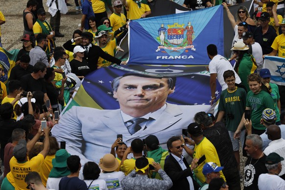 People hold a banner with a photo of Brazil&#039;s former army captain Jair Bolsonaro before the swearing-in ceremony, in front of the Planalto palace in Brasilia, Brail, Tuesday Jan. 1, 2019. Once an ...