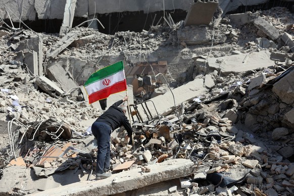 epa12794457 An Iranian man places Iran's national flag among the ruins of a damaged police station building in central Tehran, Iran, 04 March 2026. A joint Israeli and US military operation conti ...