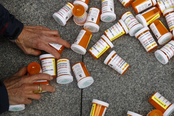 FILE - A protester gathers containers that look like OxyContin bottles at an anti-opioid demonstration in front of the U.S. Department of Health and Human Services headquarters in Washington on April  ...