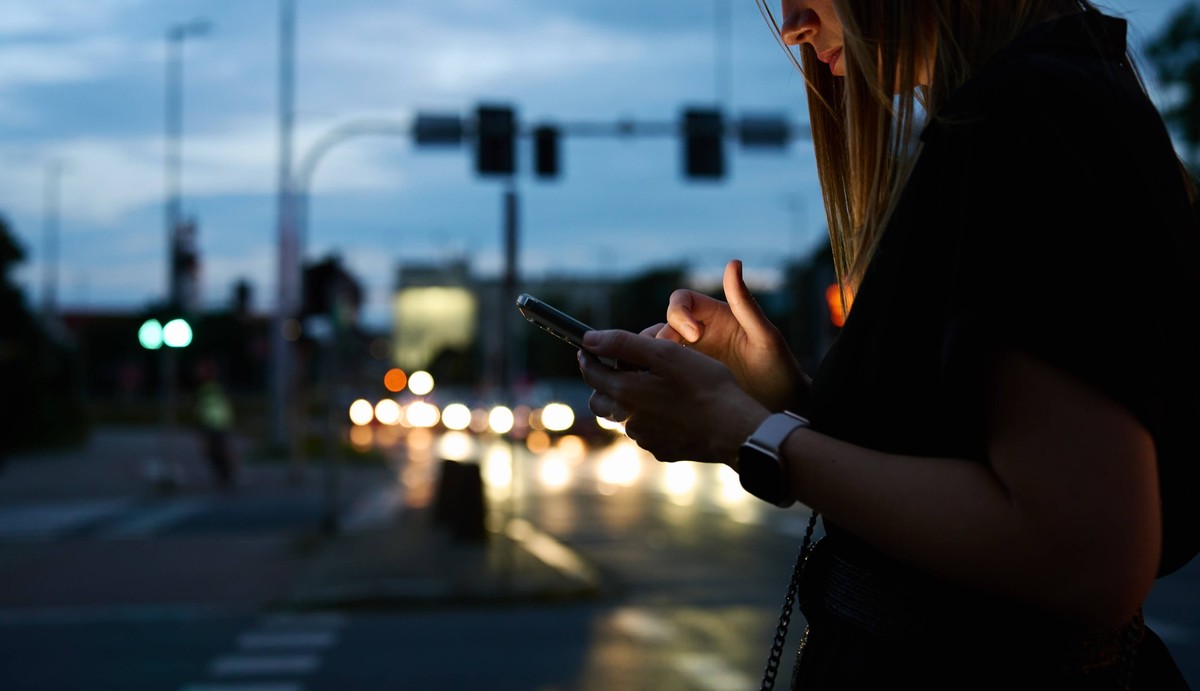 Frau benutzt Smartphone auf einer Strasse am Abend (Symbolbild)