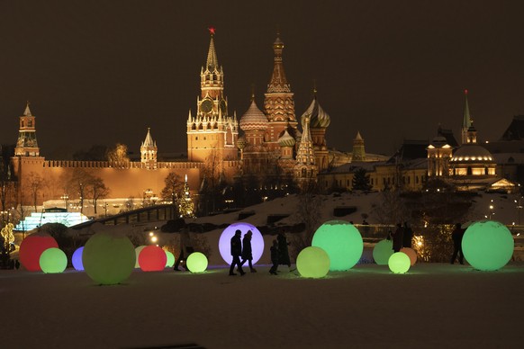 People walk at Zaryadye Park decorated for the New Year and Christmas festivities with the Kremlin Wall, the Spasskaya Tower, and the St. Basil&#039;s Cathedral in the background in Moscow, Russia, Th ...