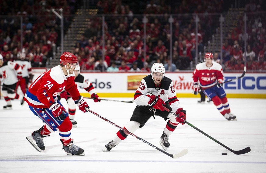 New Jersey Devils center Nico Hischier (13), from Switzerland, moves the puck past Washington Capitals defenseman John Carlson (74) during the third period of an NHL hockey game Saturday, Jan. 11, 202 ...
