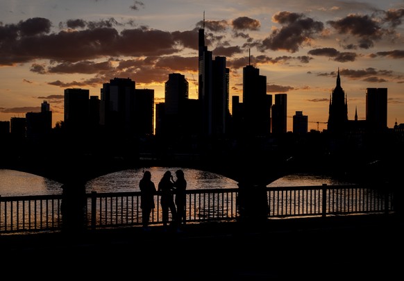 Three women stand together on a bridge over the river Main with the buildings of the banking district in background in Frankfurt, Germany, late Friday, April 10, 2020. Due to the coronavirus the econo ...