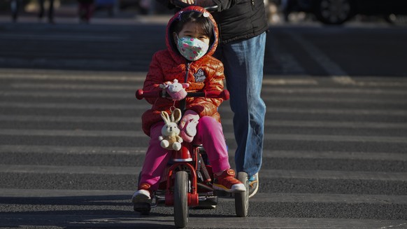 A woman pushes a child on a bicycle as they cross a street in Beijing, Wednesday, Jan. 4, 2023. The Chinese government sharply criticized COVID-19 testing requirements imposed on visitors from China a ...