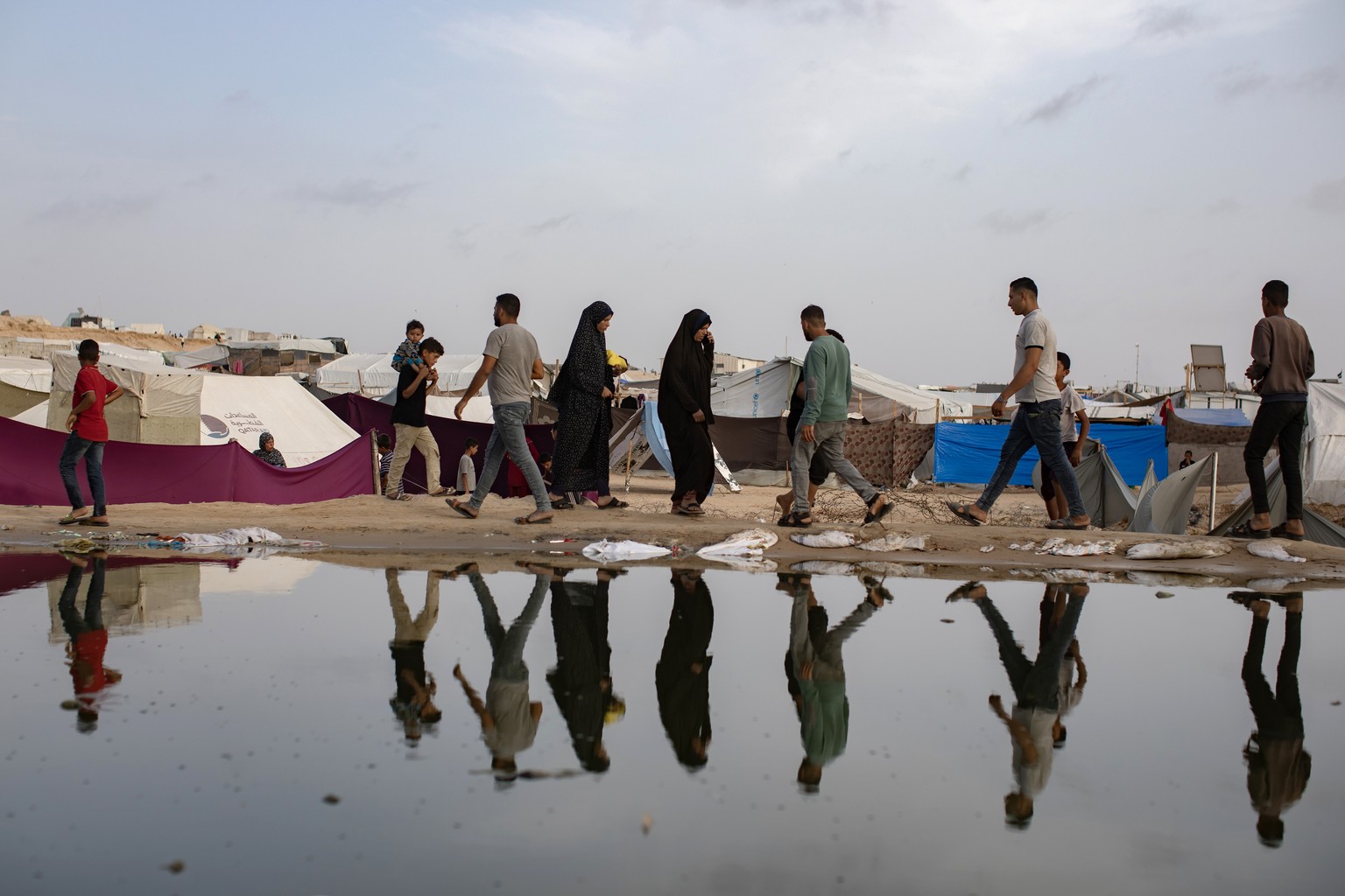 epa11303558 Palestinians walk next to a sewage spill near tents for internally displaced people at a temporary camp in Rafah camp, southern Gaza Strip, 26 April 2024. Since 07 October 2023, up to 1.7  ...