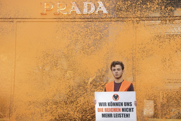 22.04.2023, Berlin: Ein Aktivist der Umweltschutzgruppe Letzte Generation h�lt vor einem Luxusgesch�ft ein Plakat. Zuvor hatte er die Fassade mit Farbe bespr�ht. �Die reichsten Deutschen emittieren ta ...