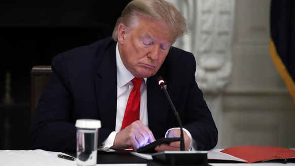 FILE - In this Thursday, June 18, 2020 file photo, President Donald Trump looks at his phone during a roundtable with governors on the reopening of America&#039;s small businesses, in the State Dining ...