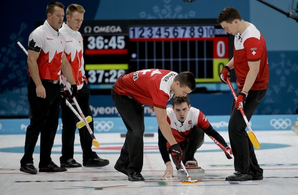 Switzerland's skip Peter de Cruz, center right, throws a stone as he watches his team sweep the ice during a men's curling match against Canada at the 2018 Winter Olympics in Gangneung, South Korea, Sunday, Feb. 18, 2018. (AP Photo/Natacha Pisarenko)