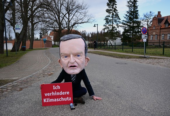 05.03.2023, Brandenburg, Gransee/Ot Meseberg: Ein als Bundesverkehrsminister Wissing kost�mierter Mann mit dem Schild &quot;Ich verhindere Klimaschutz&quot; klebt sich nahe dem G�stehaus der Bundesreg ...