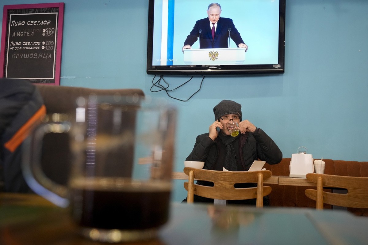 A man drinks tea sitting in a cafe under a TV screen showing Russian President Vladimir Putin during his annual state of the nation address in St. Petersburg, Russia, Tuesday, Feb. 21, 2023. (AP Photo ...