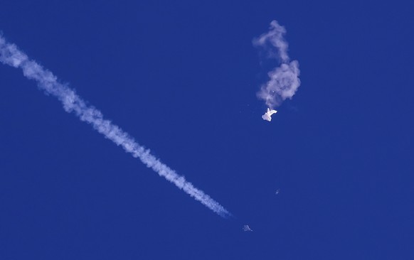 In this photo provided by Chad Fish, the remnants of a large balloon drift above the Atlantic Ocean, just off the coast of South Carolina, with a fighter jet and its contrail seen below it, Feb. 4, 20 ...