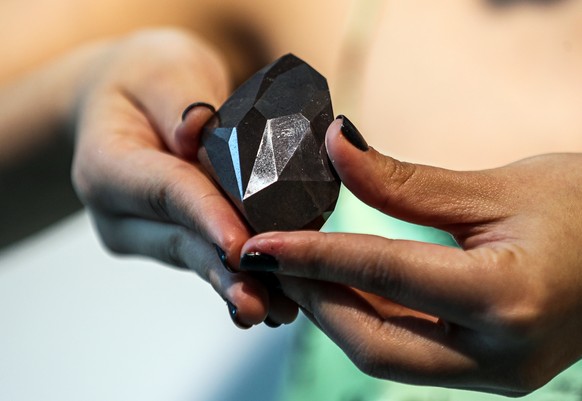 epa09690679 An employee of Sotheby&#039;s Dubai presents a 555.55 Carat Black Diamond &#039;The Enigma&#039; during the World Unveiling of Major auction highlight at Sotheby&#039;s Dubai gallery in Du ...