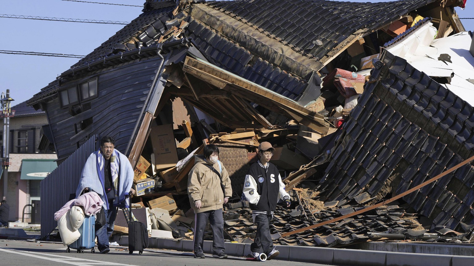 A man carries his belongings past a collapsed house following an earthquake in Wajima, Ishikawa prefecture, Japan Tuesday, Jan. 2, 2024. A series of powerful earthquakes hit western Japan, damaging bu ...