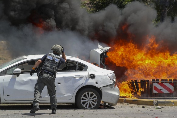 A member of Israeli bomb squad looks at burning cars that were set on fire by a missile fired from the Gaza Strip, in the southern Israeli town of Ashkelon, Tuesday, May 11, 2021. (AP Photo/Ariel Scha ...