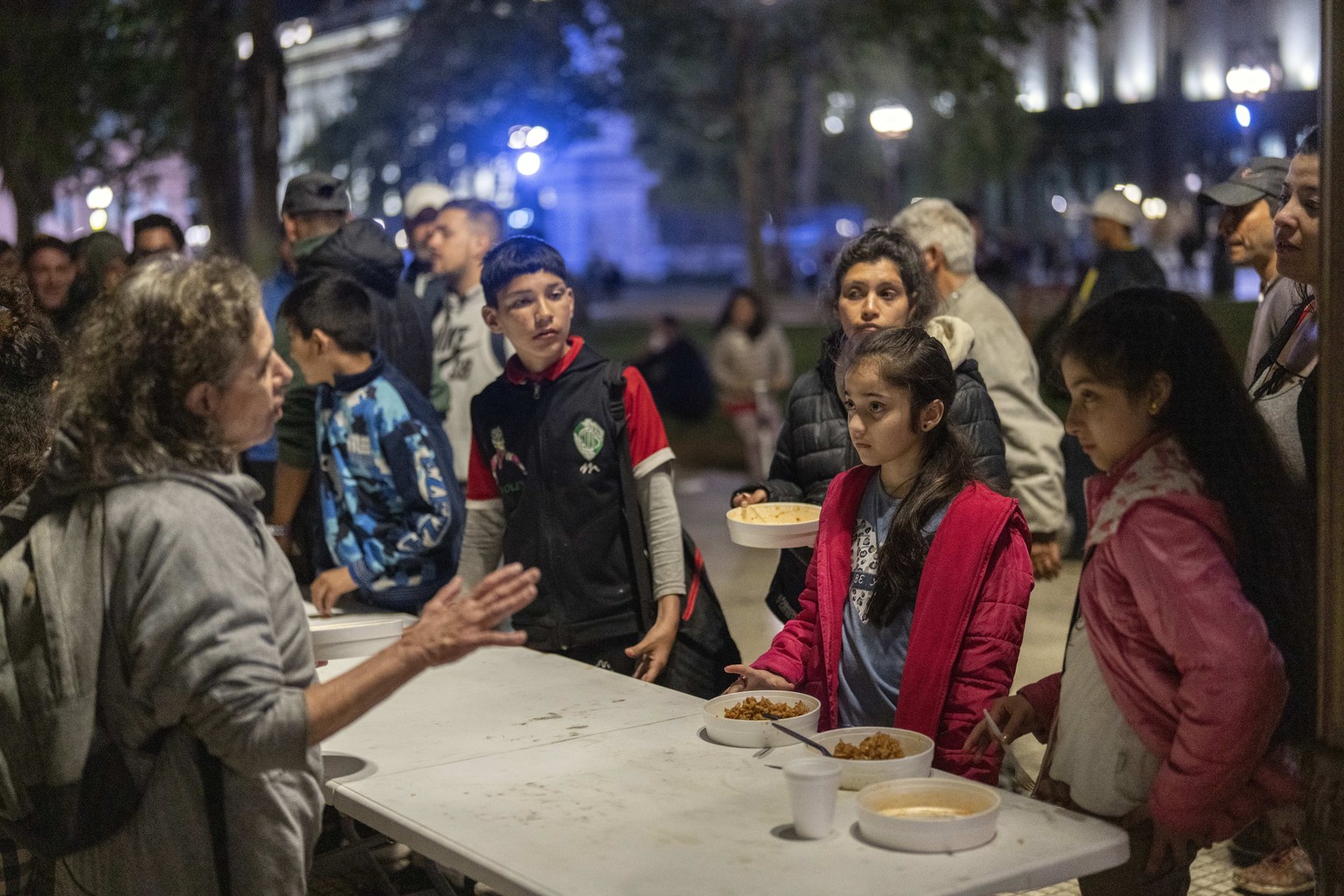 People waiting to receive meals provided by a nongovernmental organization listen to a volunteer at Plaza de Mayo square, in front of the presidential palace in Buenos Aires, Argentina, Monday, Oct. 7 ...