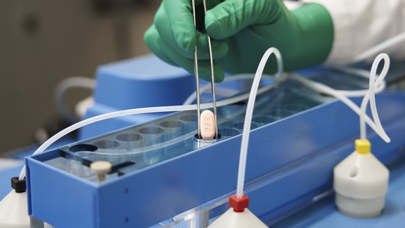 FILE - In this photo provided by Pfizer, a technician handles one of the company&#039;s COVID-19 Paxlovid pills. COVID-19 patients have two new treatment options that can be taken at home. But that co ...
