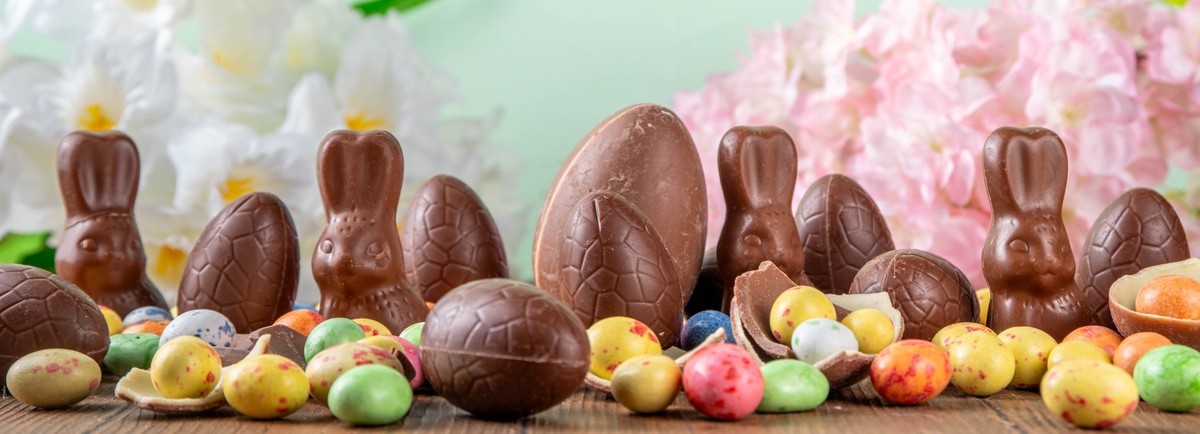 Easter background greeting card with holiday traditional confectionery, Easter egg hunt fun concept. Chocolate bunny, chocolate and candy Easter eggs on wooden background