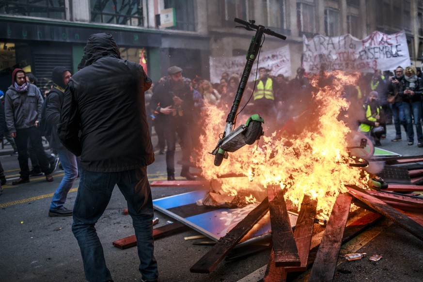 epa08092889 Protesters and &#039;Gilets Jaunes&#039; (Yellow Vests) throw scooters into a burning fire barricade during a demonstration against pension reforms lead by French Unions in Paris, France,  ...