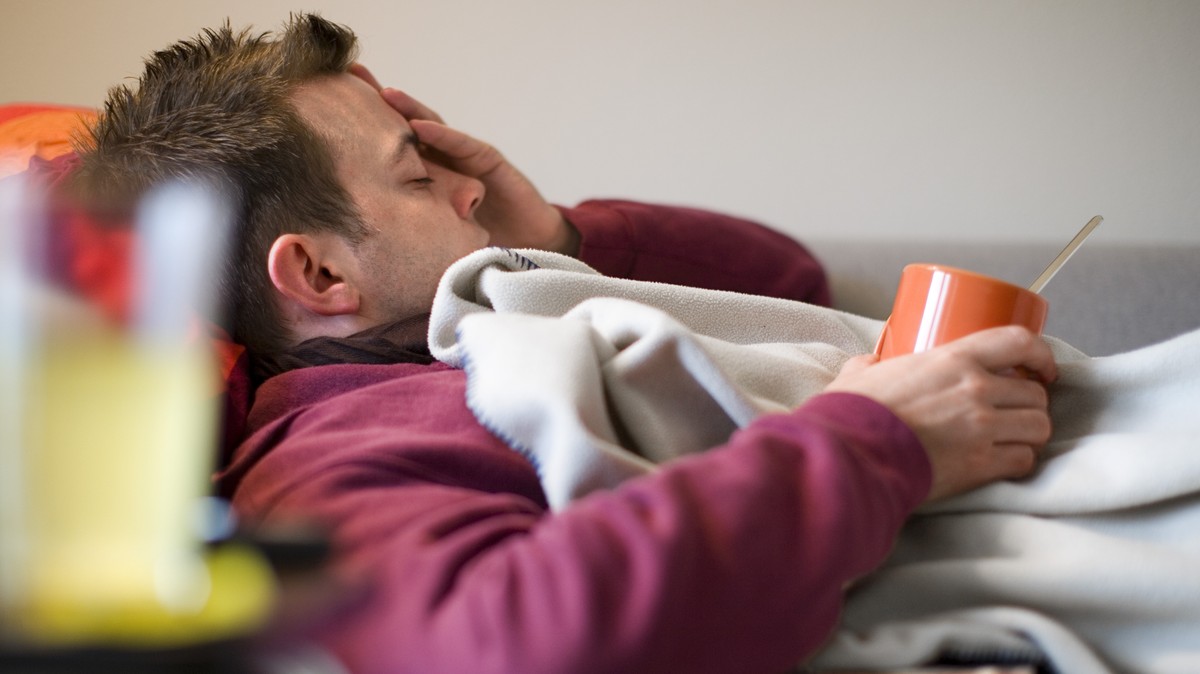 [Themenbild Grippe, gestellte Aufnahme] Ein Mann, der erkrankt ist, liegt mit einer Tasse Tee auf dem Sofa und haelt sich den schmerzenden Kopf, aufgenommen am 27. Oktober 2007 in Zuerich. (KEYSTONE/M ...