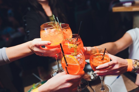 Women raising glasses of aperol spritz cocktails at the dinner table.