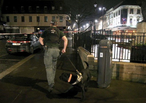 In this photo taken on Saturday, Jan. 19, 2019, a police officer with a sniffer dog are near the scene of a suspected car bomb on Bishop Street in Londonderry, Northern Ireland. Northern Ireland polit ...