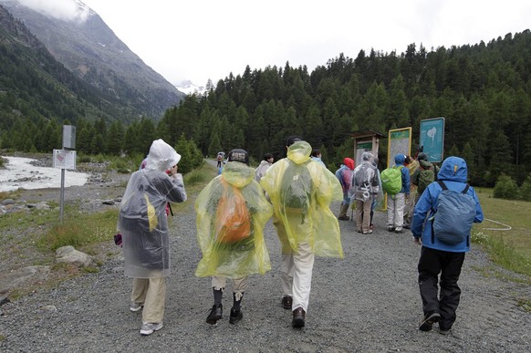Asiatische Touristen in dicker Regenbekleidung wandern am Freitag, 6. Juli 2012, bei regnerischem Wetter zum Morteratschgletscher bei Pontresina. (KEYSTONE/Arno Balzarini)