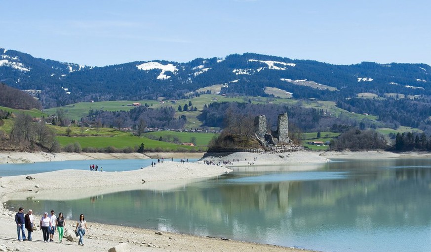 Des personnes marchent sur une bande de sable menant a la Cite d&#039;Ogoz sur le Lac de Gruyere lors d&#039;une journee de soleil ce dimanche 14 avril 2013 pres du village de Le Bry dans le canton de ...