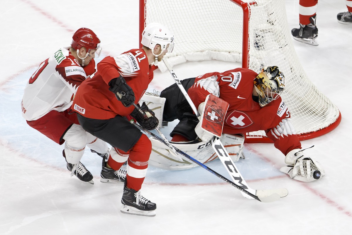 Switzerland's goaltender Reto Berra, right, tries to stop the puck past Belarus' forward Pavel Razvadovsky, left, and Switzerland's defender Mirco Mueller, center, during the IIHF 2018  ...