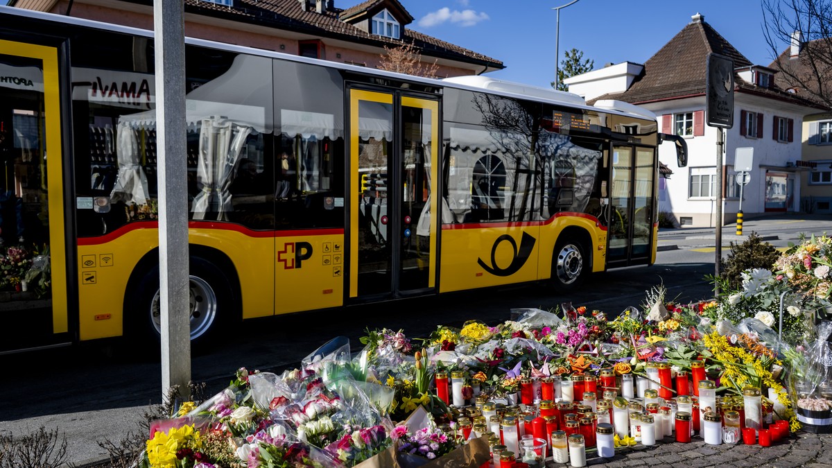 Un car postal circule devant les fleurs et les bougies deposes a l'endroit du drame, apres l'incendie d'un car postal qui a tue six personnes le jeudi 12 mars 2026 a Chietres (Kerzers)  ...