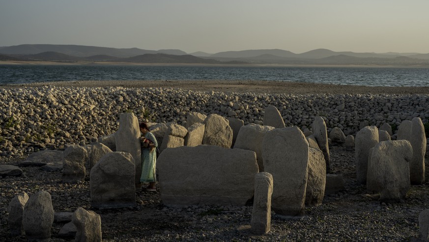 Amalie Garcia, 54, stands next to The Dolmen of Guadalperal, a megalithic monument that emerged due to drought at the Valdecanas reservoir in El Gordo, western Spain, Saturday, Aug. 13, 2022. In the w ...