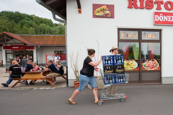 22.06.2019, Sachsen, Ostritz: Eine Frau und ein Mann schieben einen Einkaufswagen mit Bierkästen in der Nähe eines örtlichen Supermarktes auf der Straße entlang. Das ganze Bier des Supermarktes wurde  ...