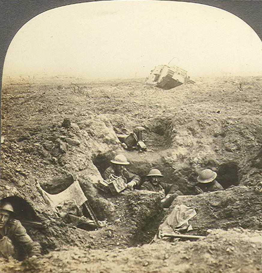 Britische Soldaten haben sich in einem Granattrichter eingegraben. Im Hintergrund ein Panzer.
