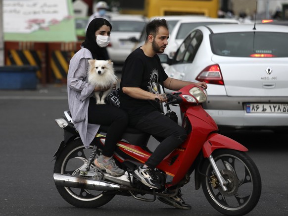 A woman holds a dog on a motorcycle while crossing an intersection in downtown Tehran, Iran, Tuesday, May 11, 2021. (AP Photo/Vahid Salemi)