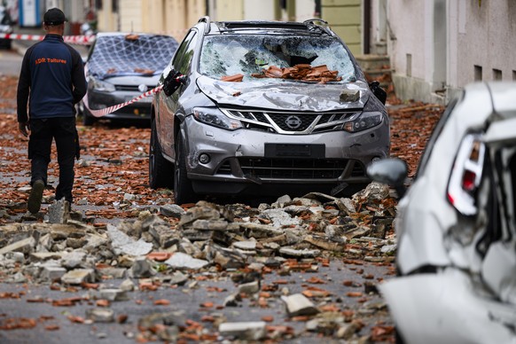 Une personne marche entre les voitures endommagees par la chute des tuiles d&#039;un toit, un jour apres la forte tempete le mardi 25 juillet 2023 a La Chaux-de-Fonds. Le deblaiement des materiaux et  ...