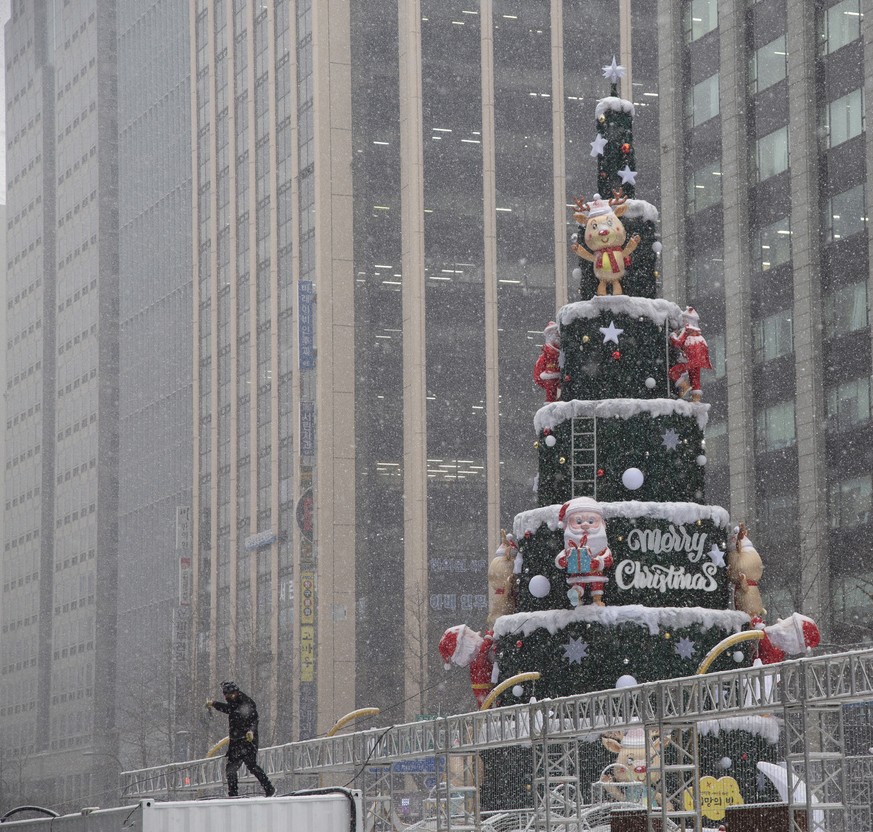 epa10366695 A worker stands next to a big Christmas tree amid snowfall on the street in Seoul South Korea, 15 December 2022. Korea Meteorological Administration (KMA) is forecasting heavy snow to hit  ...