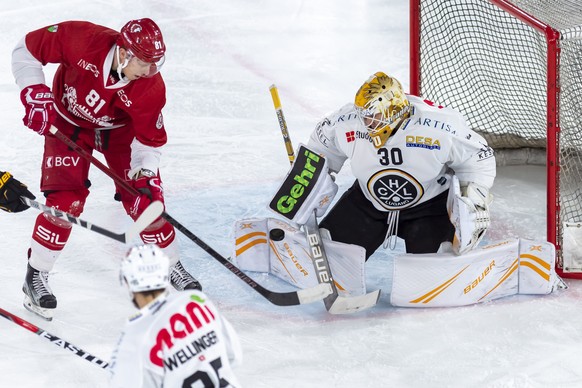 Le joueur du club lausannois, Ronalds Kenins, gauche, lutte pour le puck avec le gardien luganais, Elvis Merzlikins, droite, lors du match du championnat suisse de hockey sur glace de National League  ...