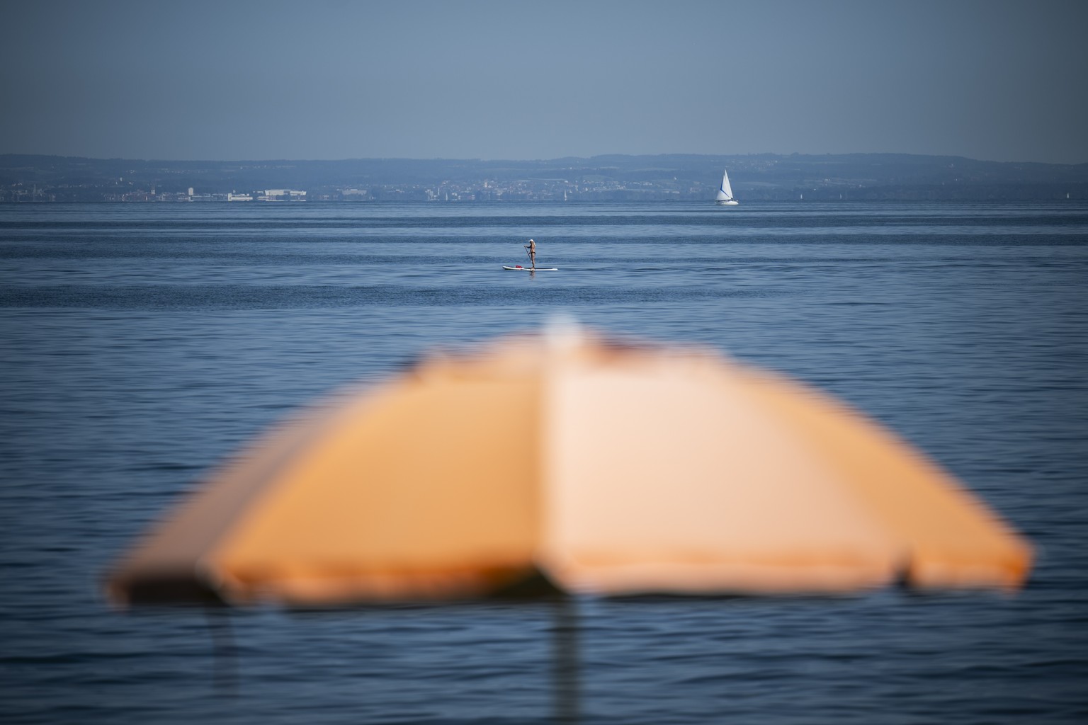 Ein Stand-Up-Paddler und Sonnenschirm, am Freitag, 18. August 2023, am Bodensee in Rorschach. Die kommenden Tage sollen grossen Teile der Schweiz eine Hitzewelle bringen. (KEYSTONE/Gian Ehrenzeller)