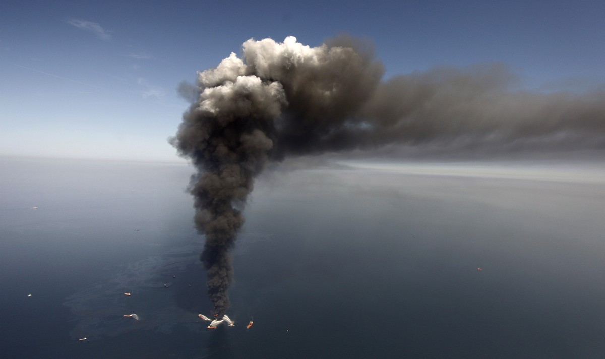 FILE - In this April 21, 2010 file photo, oil can be seen in the Gulf of Mexico, more than 50 miles southeast of Venice on Louisiana's tip, as a large plume of smoke rises from fires on BP's ...