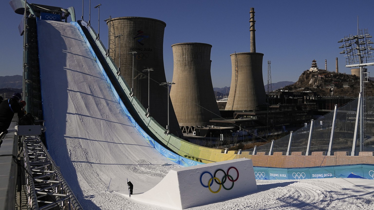 A worker shapes the kicker at the Big Air Shougang ahead of the 2022 Winter Olympics, Tuesday, Feb. 1, 2022, in Beijing, as the old cooling towers of a steel plant stand in the city&#039;s former indu ...