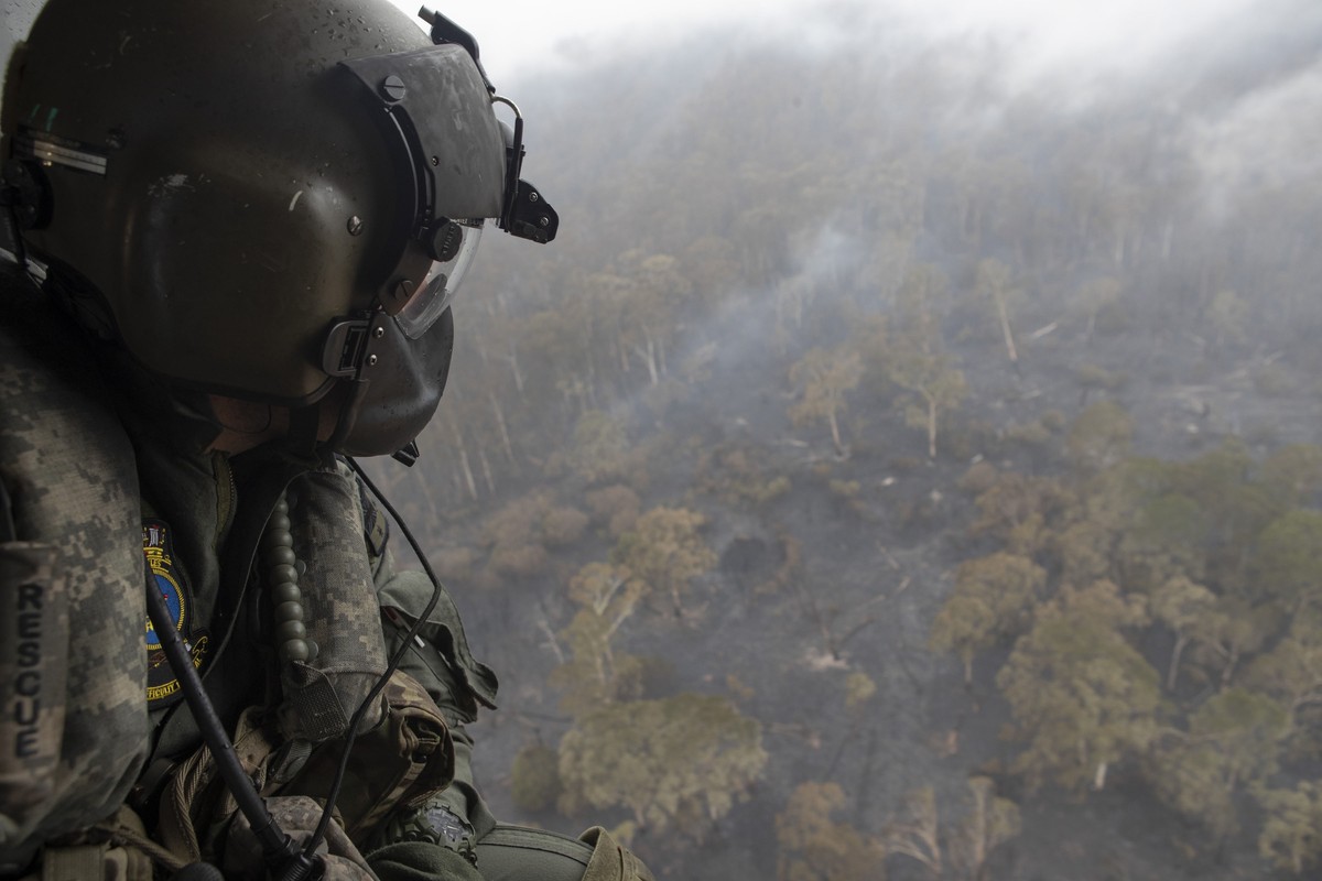 epa08109253 A handout photo made available by Australia's Department of Defence on 07 January 2020 shows leading seaman aircrew Brendan Menz looking out the door of HMAS Choules' MRH-90 Mari ...